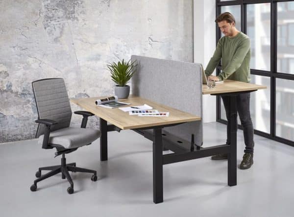 Duo zit sta bureau met een zwart onderstel, lichte bureaubladen en een grijs akoestisch paneel.