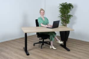 Vrouw in een groen pak zit lachend achter een sta bureau.