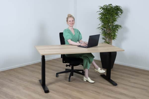 Vrouw in een groen pak zit lachend achter een sta bureau.
