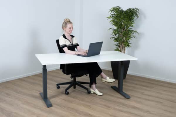 Vrouw met een zwart wit pak zit achter een wit bureau.