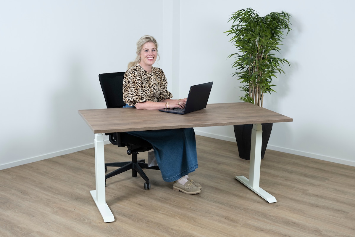 Vrouw met een blauwe rok zit achter een sta bureau met haar laptop.