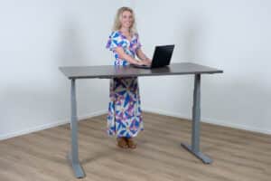 Vrouw staat achter een elektrisch bureau met een aluminium poot en een donker eiken blad.