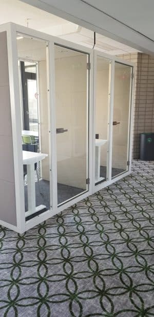 Kantoorruimte met daarin twee geluidsdichte cabines. Ze hebben een wit metalen frame en witte sta bureaus erin. Dit is de akoestische stilte werkplek voor 1 persoon SIL03.