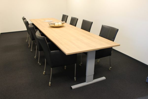 Vergaderruimte met daarin een goedkope, rechthoekige vergadertafel. Deze heeft een aluminium poot en een licht blad. Eromheen staan acht vergaderstoelen.