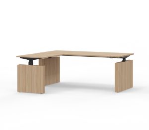 Witte achtergrond met daarvoor een L-bureau. Dit hoekbureau is van licht hout en heeft om de drie poten wangen. Deze is elektrisch verstelbaar.