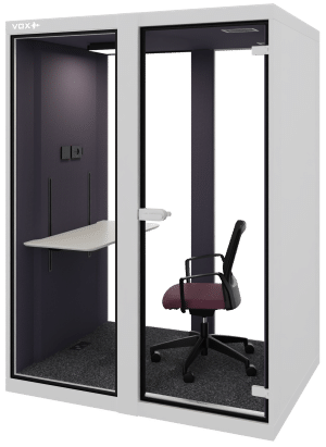 Grijze achtergrond met daarvoor de akoestische cabine VOX Medium. Deze is wit aan de buitenkant en heeft een zwarte binnenkant. Erin staat een werktafel en een bureaustoel. Dit is een akoestische werkplek.