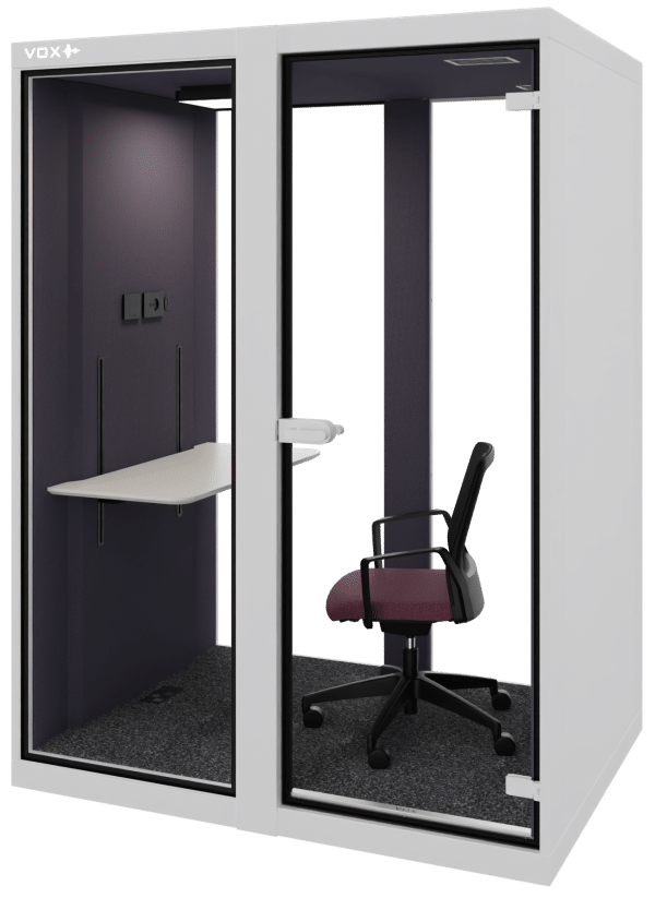 Grijze achtergrond met daarvoor de akoestische cabine VOX Medium. Deze is wit aan de buitenkant en heeft een zwarte binnenkant. Erin staat een werktafel en een bureaustoel. Dit is een akoestische werkplek.