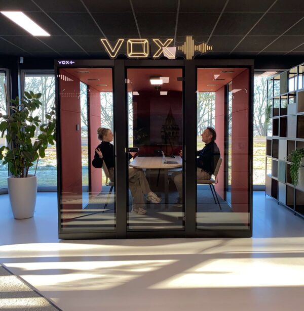 Zwarte vergadercabine met rode binnenkant, twee mensen overleggen erin.