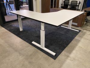 Een showroom met daarin een wit tweedehands hoekbureau. Dit is het Twinform hoekbureau. Eronder zitten drie poten in het wit.