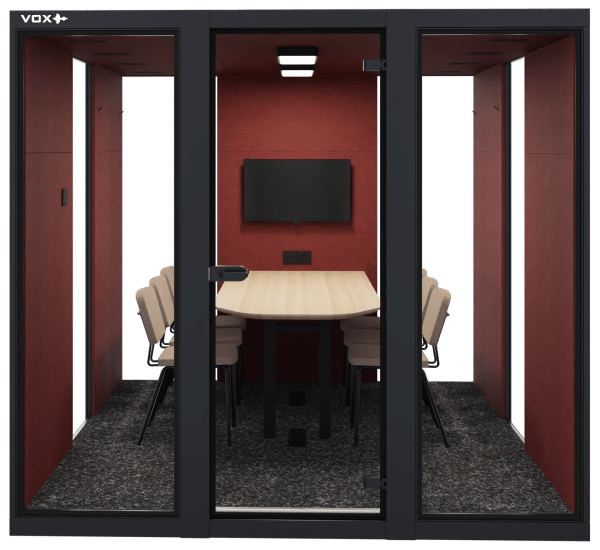 Geluidsdichte cabine met rood akoestisch materiaal op de muren, een lichthouten tafel en daaromheen zes stoelen. Tegen de muur hangt ook een beeldscherm. Dit is de VOX XLarge.