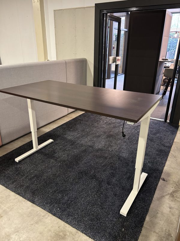 Een gebruikt hoog laag bureau staat in de showroom. Deze heeft een wit onderstel en een donker houten blad.