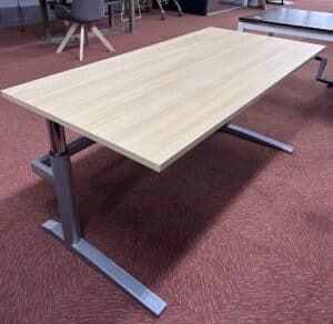 Gebruikt slinger verstelbaar bureau met een licht blad en aluminium onderstel. Het bureau staat in een ruimte met een rode vloer.