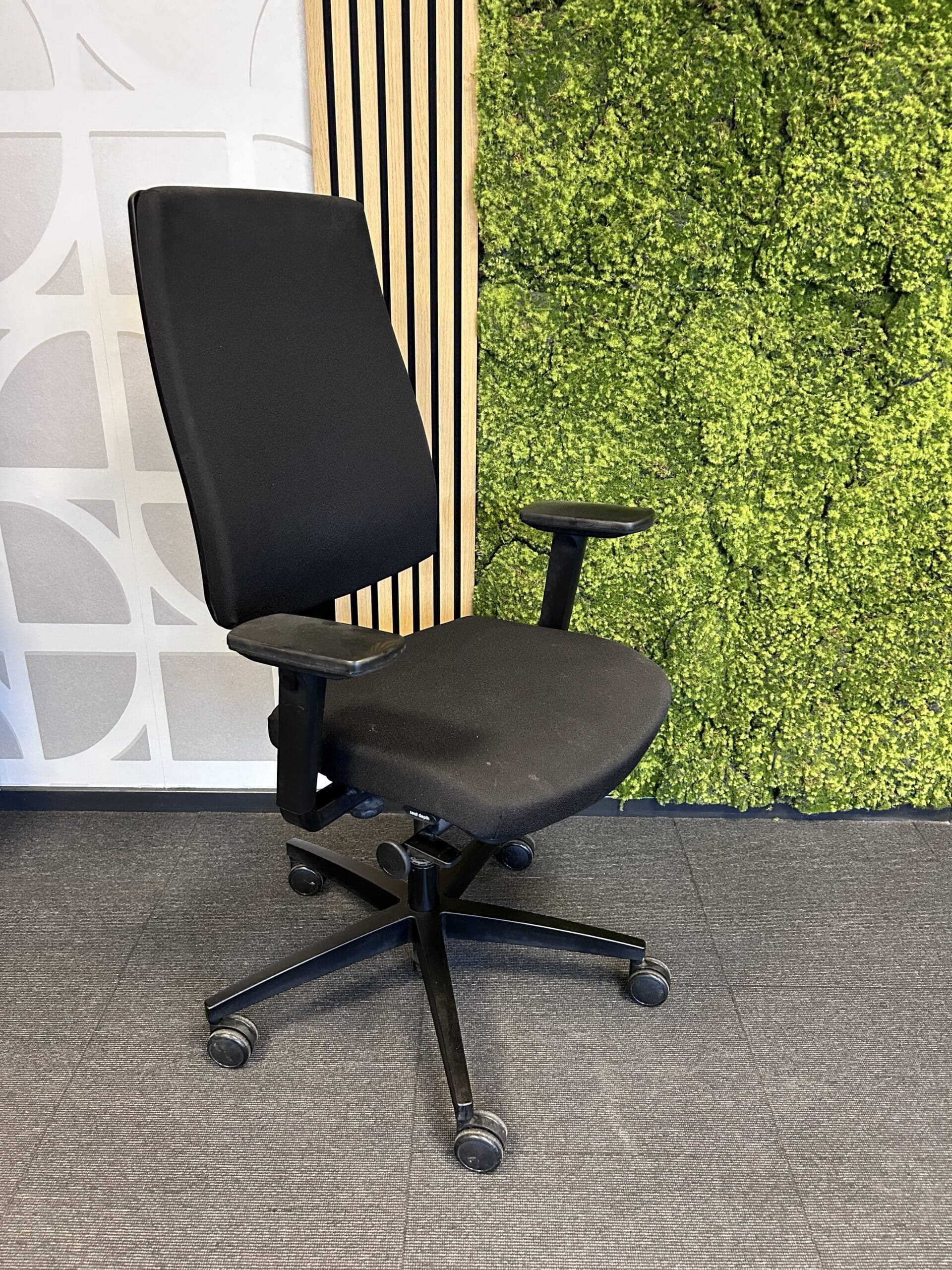 Tweedehands bureaustoel Bèta Be Sure in de kleur zwart. De stoel staat in een kantoor met een grijze vloer en groene moswand.
