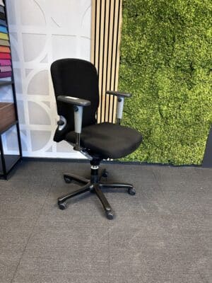 Zwarte tweedehands Haworth Comforto bureaustoel met een zwarte voet, in een kantoorruimte met grijze vloeren en moswand.