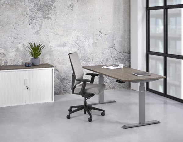 een grijze bureaustoel achter een bureau met grizje poten en een houten blad in een kamer met daarin een schuifdeurkast Elektrisch zit sta bureau 140 x 80 professional
