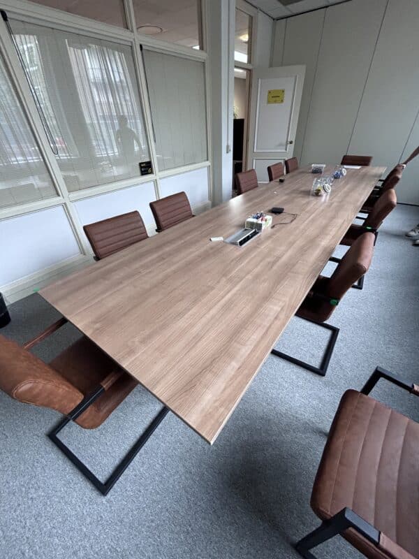 Vergaderruimte met daarin een grote vergadertafel. Deze heeft een houtkleur blad en er staan leren vergaderstoelen omheen. Het is de tweedehands vergadertafel van 240x120 cm.
