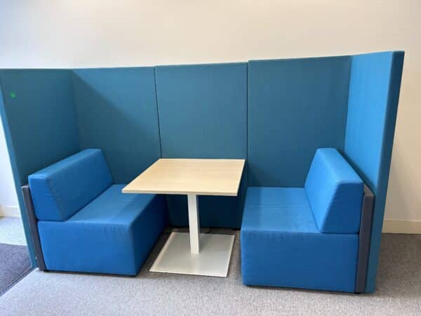 Kantoorruimte met daarin een blauwe treinbank. Deze heeft hoge akoestische panelen, met daarin twee blauwe treinbanken en daar tussenin weer een witte tafel. Dit is de akoestische tweedehands treinbank van König + Neurath.