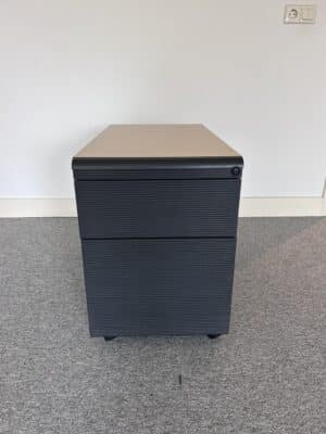 Kantoorruimte met grijze vloerbedekking waar een zwart ladeblok op staat. Deze heeft drie lades en een licht houten bovenkant. Dit is het gebruikt zwart ladeblok Mezzo.