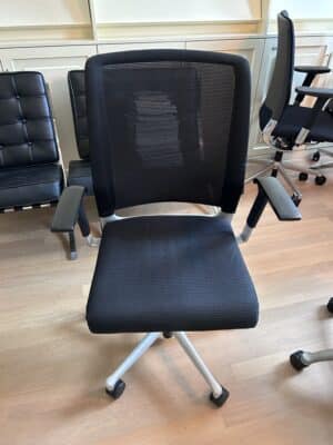Kantoorruimte met daarin een zwarte bureaustoel, met een netweave rugleuning en een aluminum kruisvoet. Dit is de gebruikte bureaustoel Interstuhl.