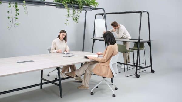 Ruimte met een hoge vergadertafel erin en een grote vergadertafel ervoor. Deze heeft planten op het frame.