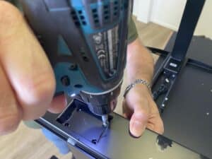 Een hand schroeft met een boormachine de voeten vast aan de poten van het bureau. 