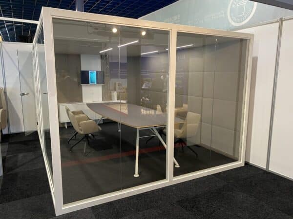 Vergadercabine met wit metalen frame en vergadertafel en -stoelen erin.
