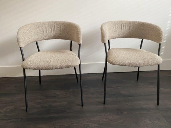 Twee gebruikte eetkamerstoelen met een taupe stoffering en zwart metalen frame.