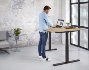 Man werkt staand achter een hoekbureau met zwart onderstel en licht houten blad.