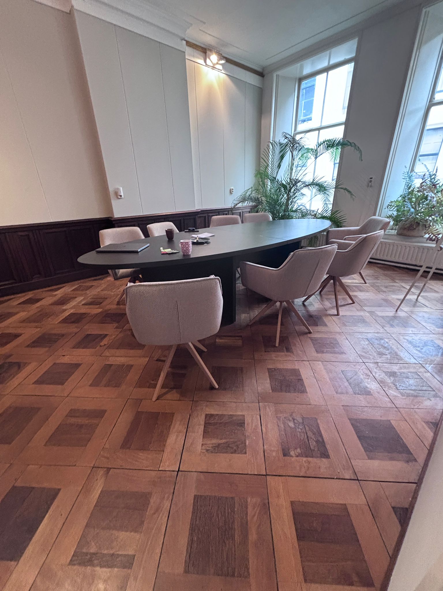 Monumentaal pand met zwarte vergadertafel en zandkleurige vergaderstoelen.