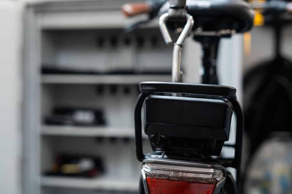 Op voorgrond achterkant accu elektrische fiets, achtergrond openstaande accukast